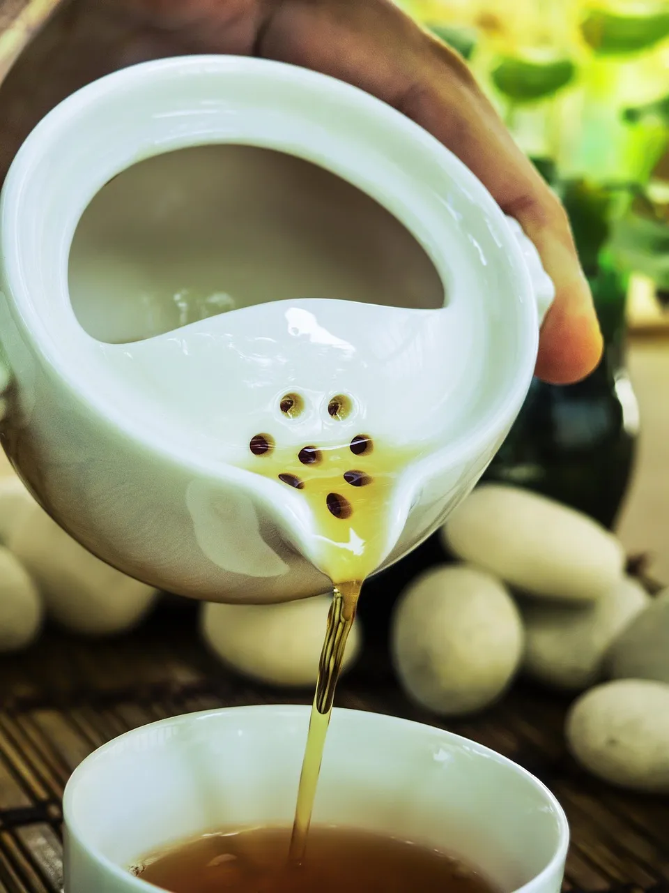 Pale tea being poured through a white porcelain strainer