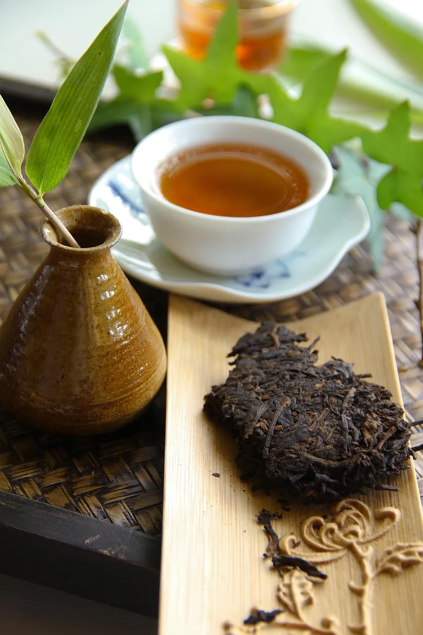 A piece of compressed pu-erh tea cake beside a cup of dark tea